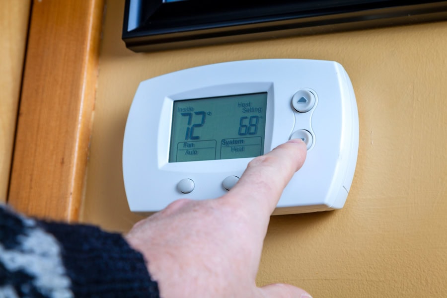 Should I Select “On” or “Auto” Fan Setting on My Thermostat? A person lowers temperature on a home thermostat. Energy saving concept.